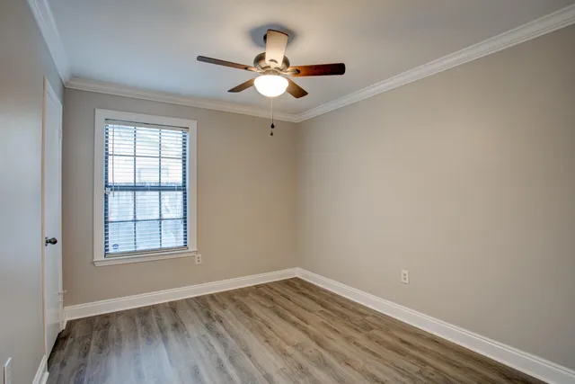 an empty room with wooden floor chandelier fan and windows
