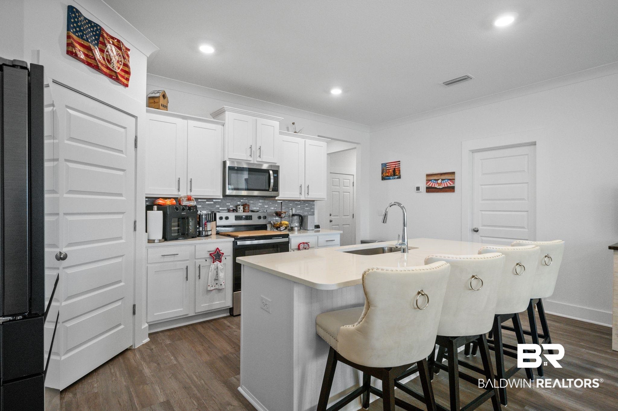 8508 Rosedown Lane Daphne, AL 36526 - Photo 12 of 29 Kitchen featuring a kitchen bar, white cabinetry, stainless steel appliances, decorative backsplash, and dark wood-style flooring