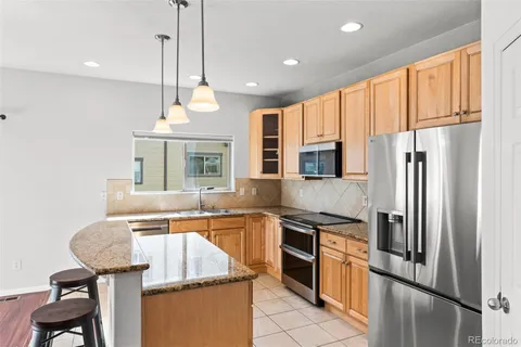 a kitchen with stainless steel appliances granite countertop a refrigerator a sink dishwasher a stove and a dining table with wooden floor
