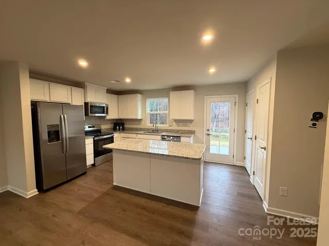 a kitchen with stainless steel appliances granite countertop a refrigerator a sink dishwasher a stove and white countertops with wooden floor