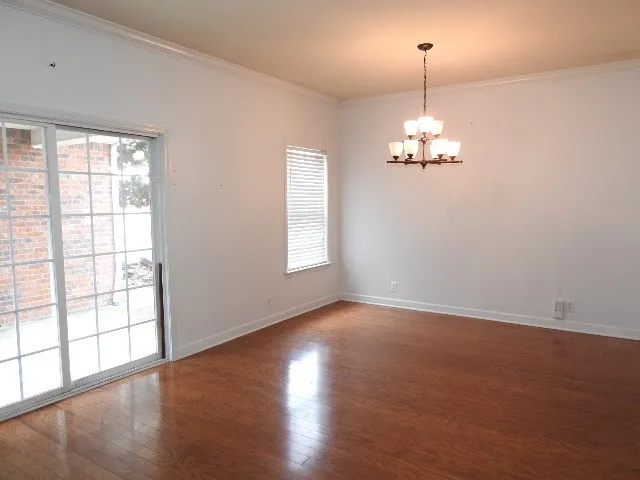 an empty room with wooden floor chandelier and windows