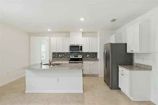 a kitchen with kitchen island granite countertop stainless steel appliances a refrigerator a stove top oven and white cabinets