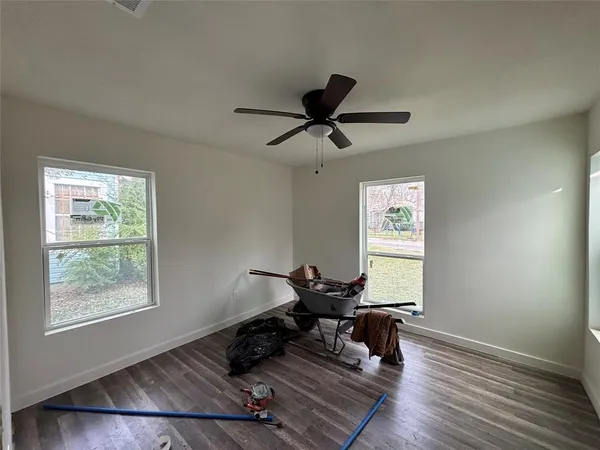 an empty room with wooden floor a ceiling fan and windows