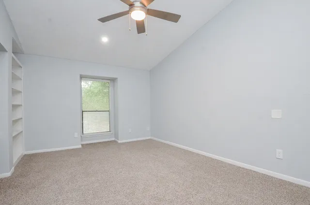 an empty room with a chandelier fan and windows