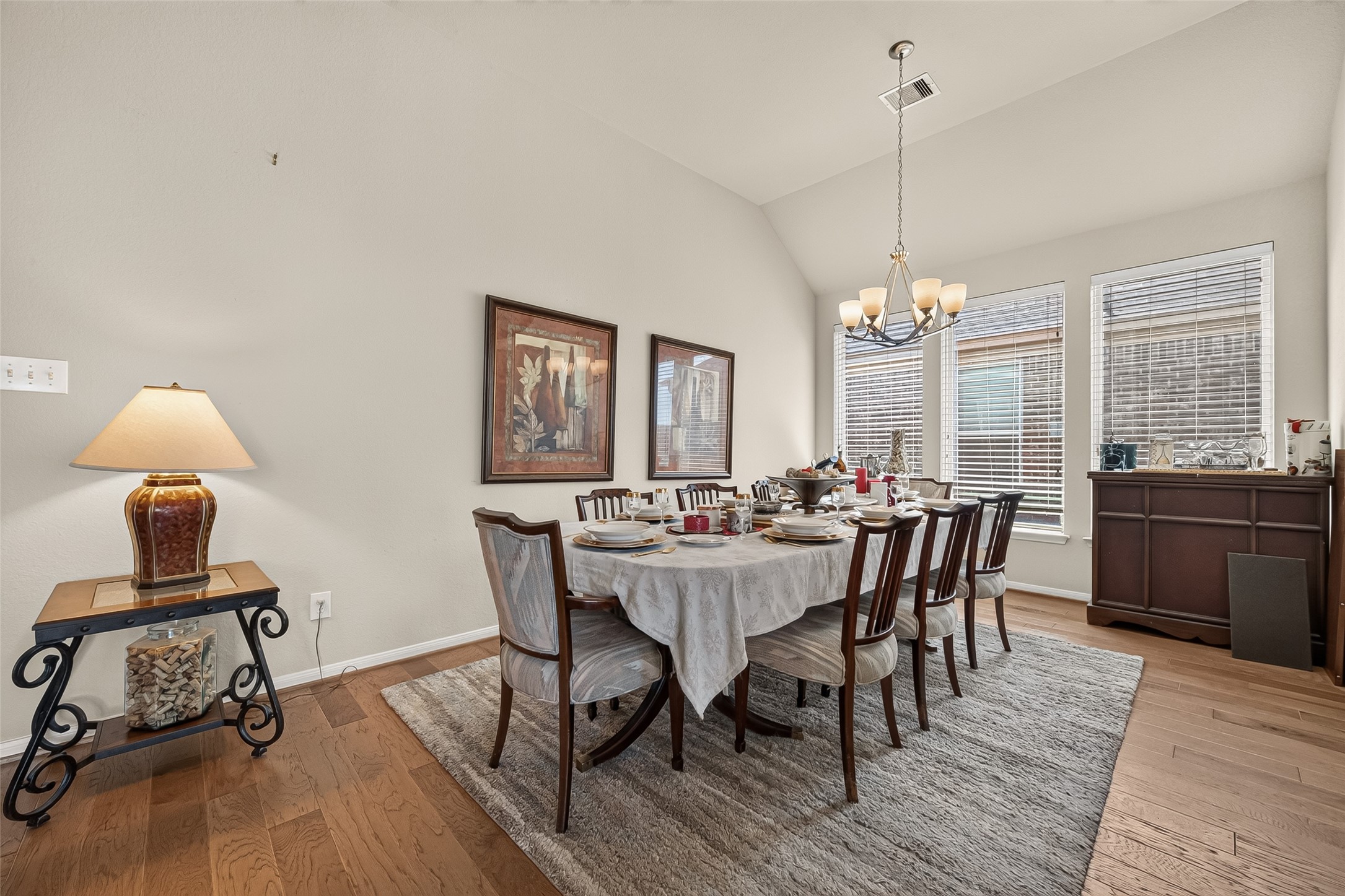 4910 Culver Lane Rosenberg, TX 77471 - Photo 23 of 50 This dining room features a spacious table set for eight, with elegant decor and a neutral color palette. Natural light fills the room through large windows, enhancing the warm wood flooring and stylish chandelier.
