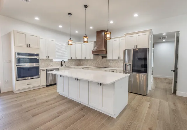 a large kitchen with stainless steel appliances kitchen island granite countertop a refrigerator a oven a island and white cabinets with wooden floors