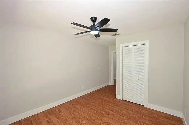 an empty room with wooden floor and a ceiling fan