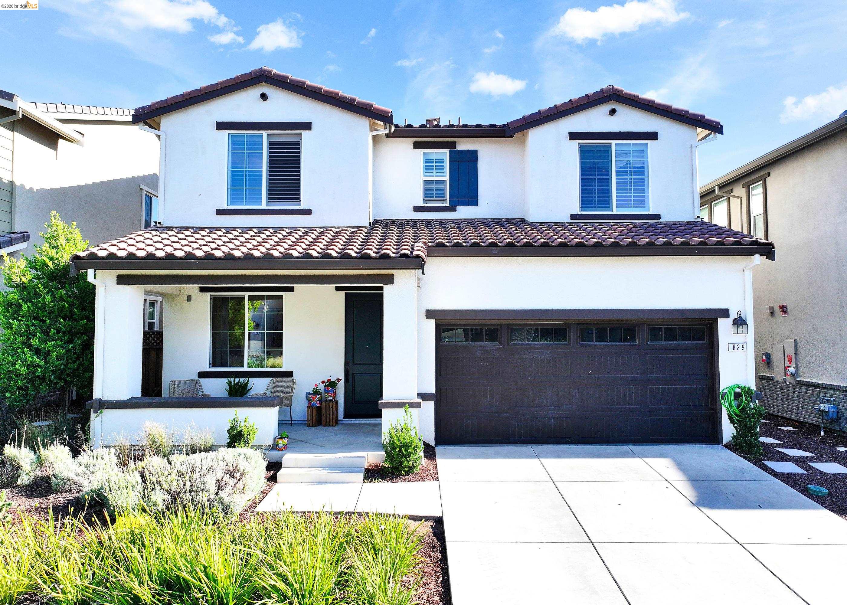 Stucco exterior with dark trim accents, tile roof, attached garage, and a covered front porch