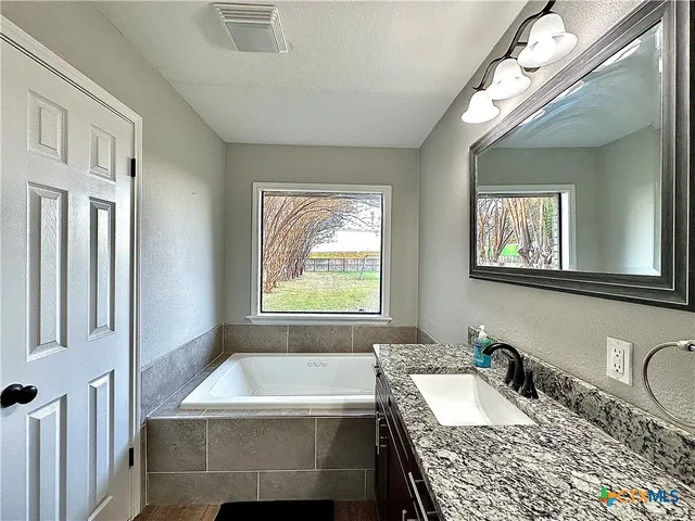 a bathroom with a granite countertop tub a sink and a window