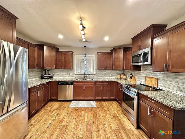 a large kitchen with stainless steel appliances granite countertop a stove refrigerator sink and cabinets