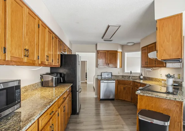 a kitchen with stainless steel appliances granite countertop wooden cabinets a sink dishwasher a stove and a refrigerator with wooden floor