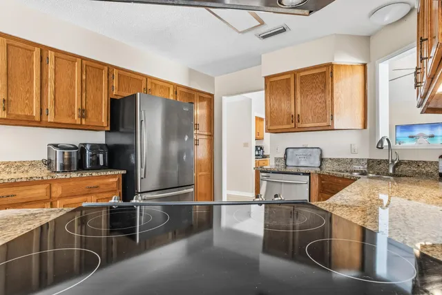 a kitchen with stainless steel appliances granite countertop a refrigerator a stove and a sink with wooden cabinets