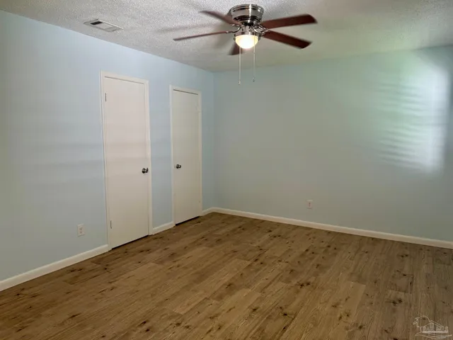 an empty room with wooden floor fan and windows