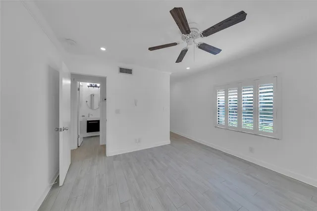 a view of an empty room with wooden floor and a ceiling fan