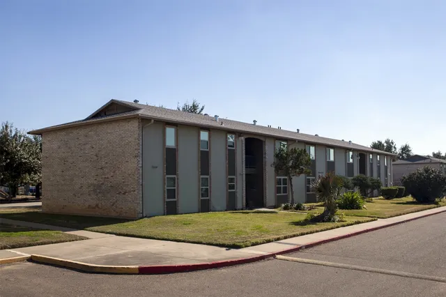 a view of a brick house with a small yard and a large parking space