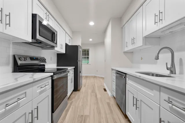 a kitchen with stainless steel appliances granite countertop a sink a stove top oven a refrigerator with wooden cabinets and floor