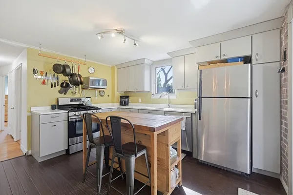 a kitchen with stainless steel appliances granite countertop a refrigerator a sink a stove a dining table and chairs with wooden floor