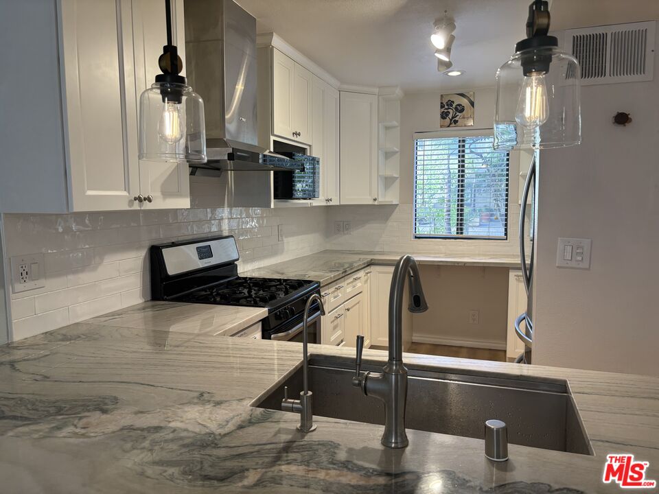 557 East Verdugo Avenue, Unit C Burbank, CA 91501 - Photo 11 of 14 a kitchen with stainless steel appliances kitchen island granite countertop a sink dishwasher a stove and white cabinets with wooden floor