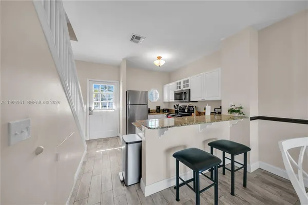 a kitchen with stainless steel appliances granite countertop a refrigerator a stove a sink dishwasher and white cabinets with wooden floor