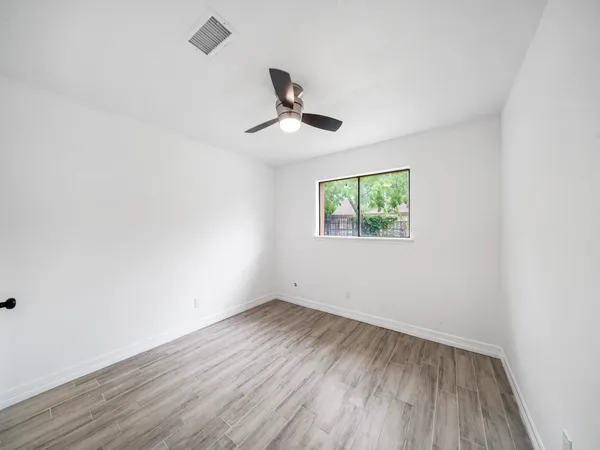 an empty room with wooden floor ceiling fan and windows