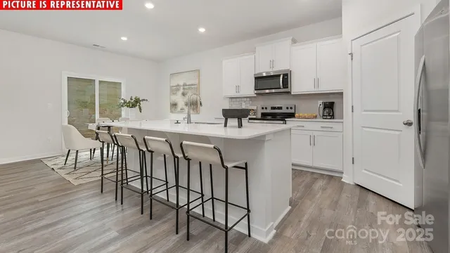 a kitchen with stainless steel appliances granite countertop a stove a sink a microwave a refrigerator with white cabinets and wooden floor