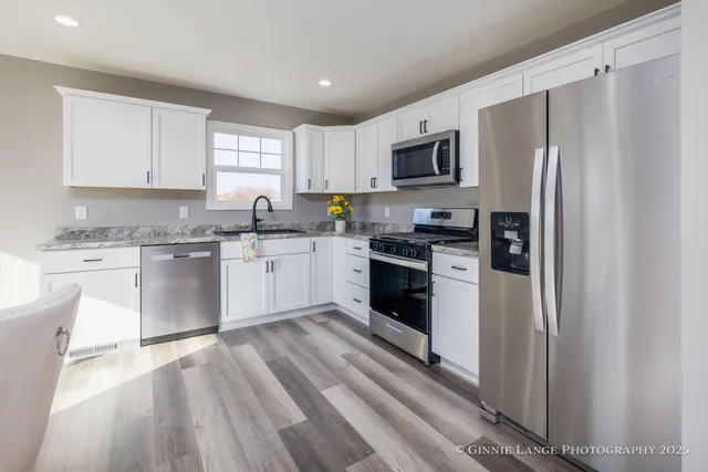 a kitchen with stainless steel appliances granite countertop a refrigerator a stove top oven a sink dishwasher and white cabinets with wooden floor