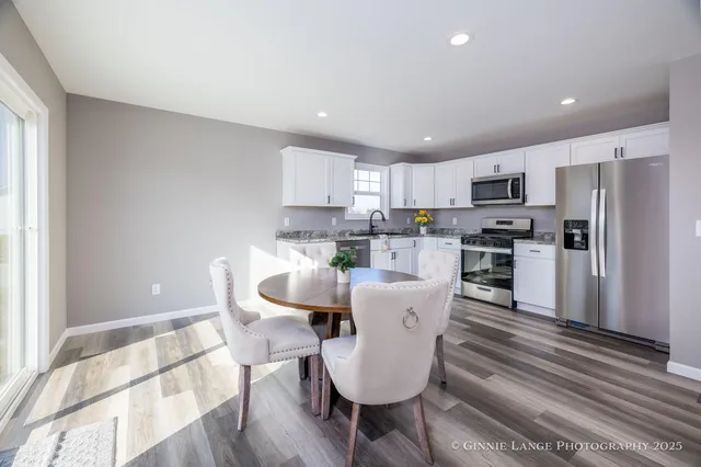 a living room with stainless steel appliances a dining table wooden floor and a view of kitchen