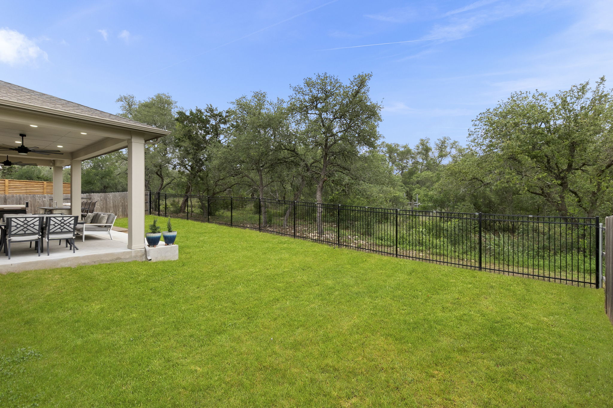 460 Constitution Way Kyle, TX 78640 - Photo 36 of 40 Expansive lawn area featuring a covered patio, black metal fencing, wood privacy fencing, and mature trees
