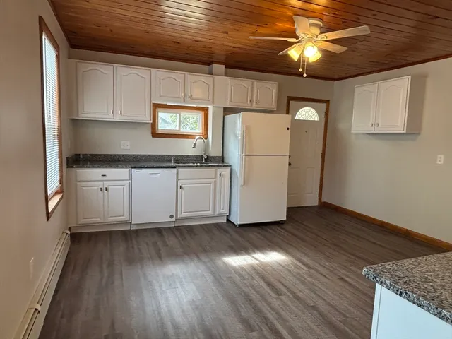 a kitchen with granite countertop a stove a sink and white cabinets with wooden floor
