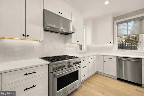 a kitchen with stainless steel appliances granite countertop white cabinets a sink a stove a microwave and wooden floors