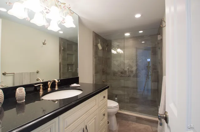 a bathroom with a granite countertop sink a toilet a mirror and shower