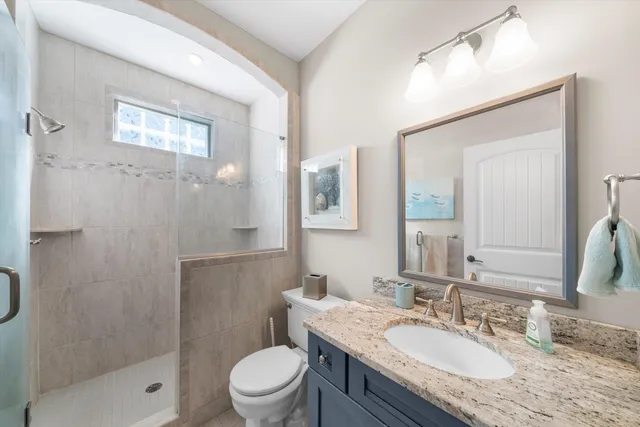 a bathroom with a granite countertop sink a toilet a mirror and shower