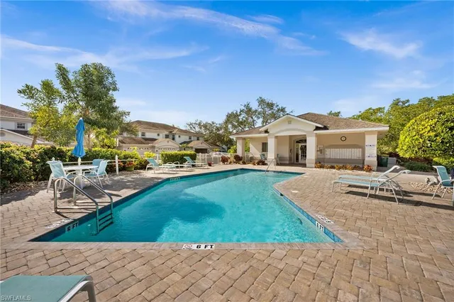 a view of a white house next to a yard with potted plants and palm trees