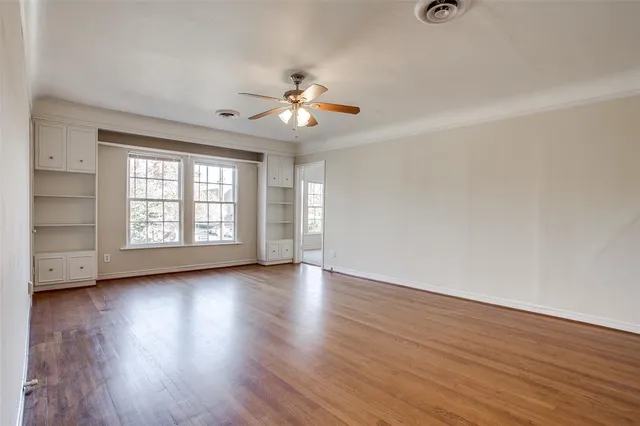 an empty room with wooden floor chandelier fan and windows