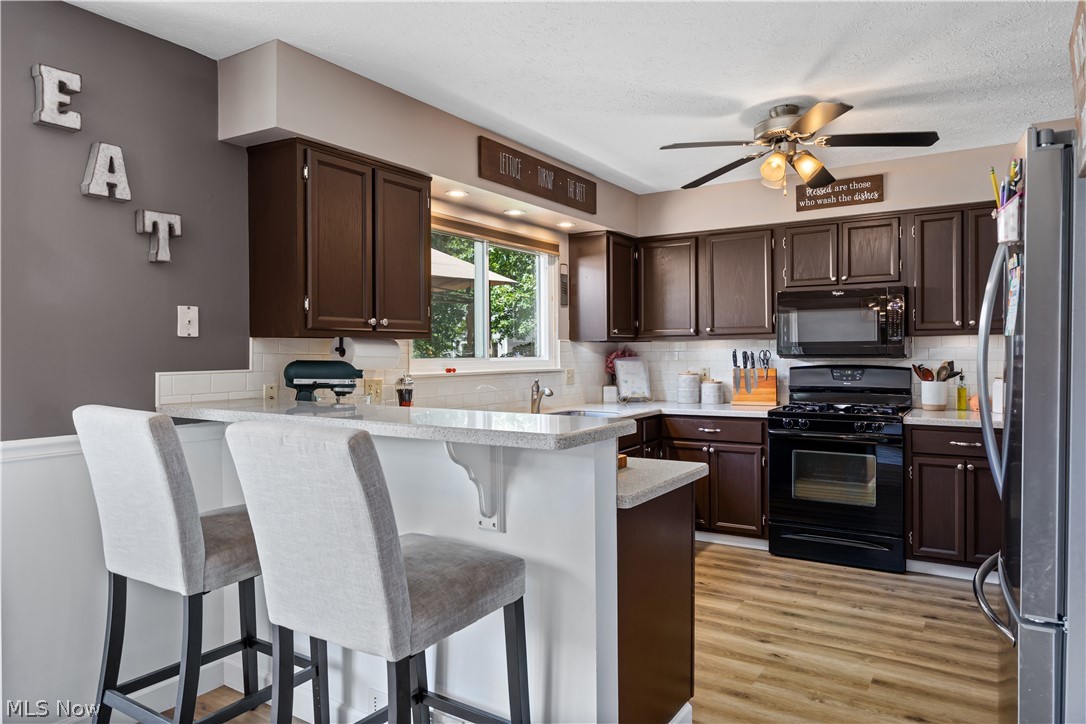 684 Guilford Road Vermilion, OH 44089 - Photo 17 of 37 Kitchen with black appliances, decorative backsplash, a kitchen bar, light hardwood / wood-style floors, and kitchen peninsula