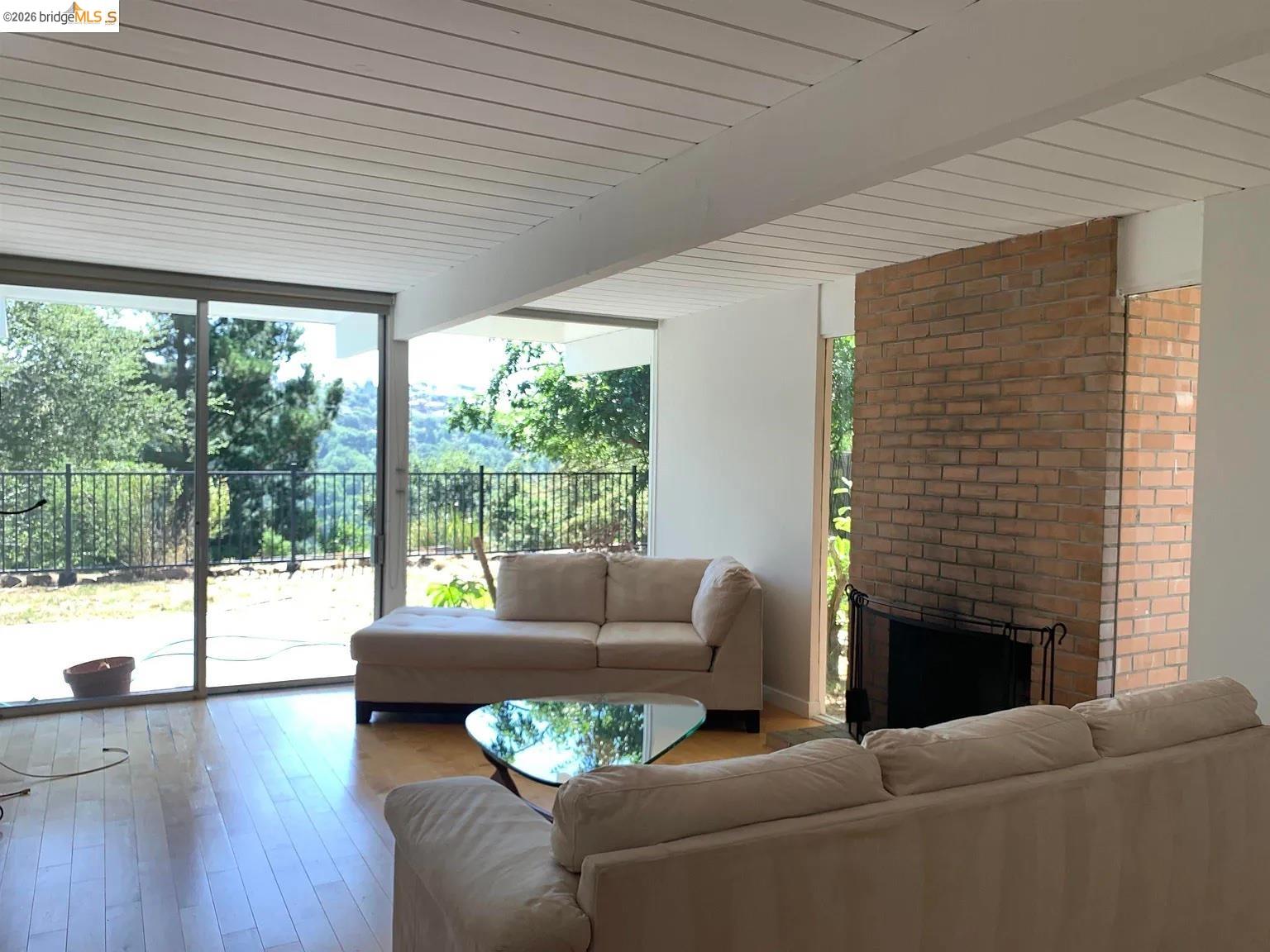5559 Greenridge Road Castro Valley, CA 94552 - Photo 22 of 33 Living area featuring beamed ceiling, expansive windows, plenty of natural light, a brick fireplace, and hardwood / wood-style flooring