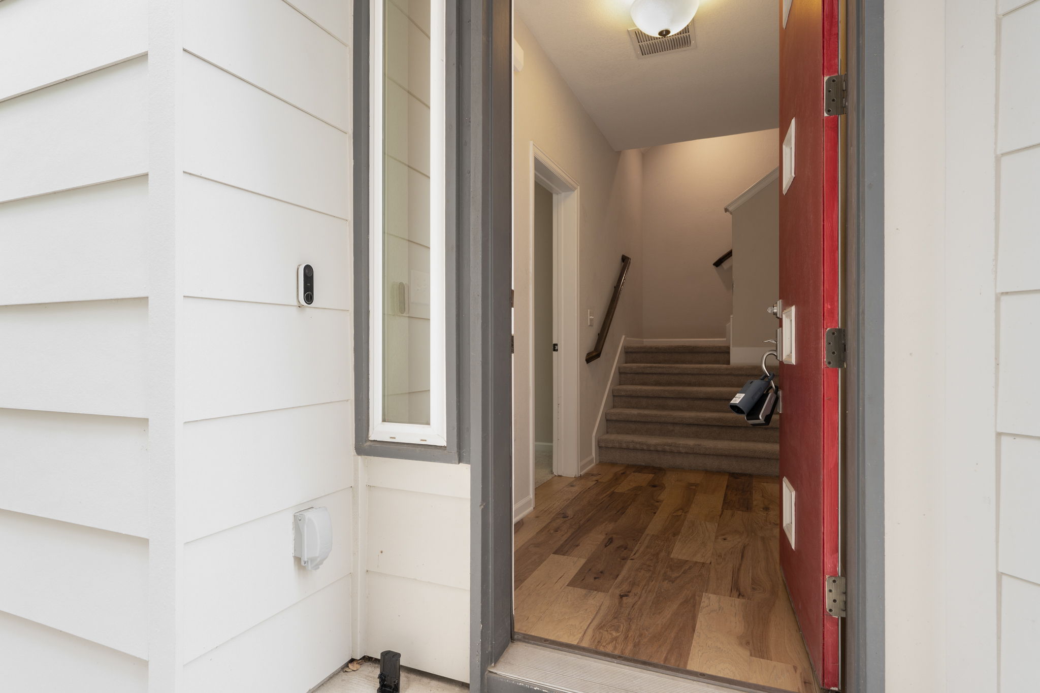 4403 Swift Path Austin, TX 78741 - Photo 26 of 32 Inviting entry featuring a red paneled door, wood-finish flooring, white horizontal siding, and a vertical sidelight window