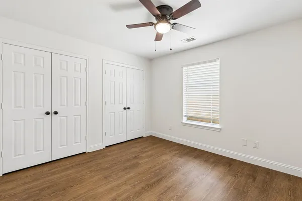 an empty room with wooden floor chandelier fan and windows