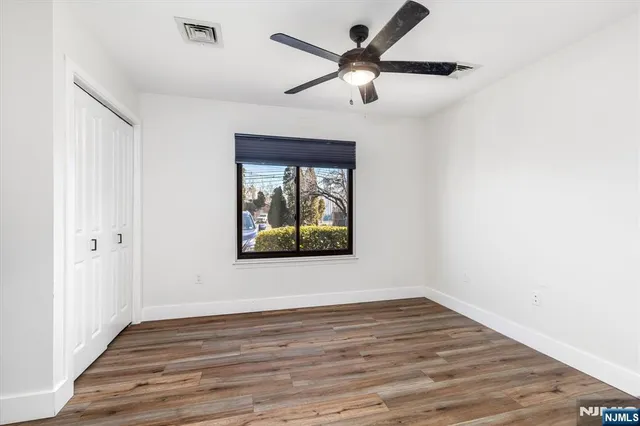 an empty room with wooden floor ceiling fan and windows