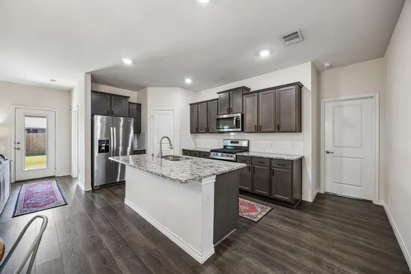 a kitchen with stainless steel appliances granite countertop a stove top oven a refrigerator a sink and dishwasher with wooden floor