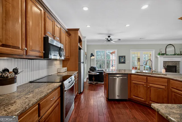 a kitchen with stainless steel appliances granite countertop wooden cabinets a sink dishwasher a stove and a refrigerator with wooden floor