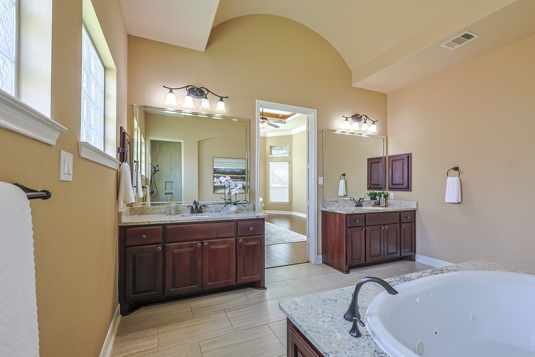 515 Mill Creek Road Pinehurst, TX 77362 - Photo 27 of 48 This spacious bathroom features dual vanities with granite countertops, elegant lighting, and a large jacuzzi tub. Natural light streams through frosted windows, and the open doorway leads to a bright adjoining bedroom.
