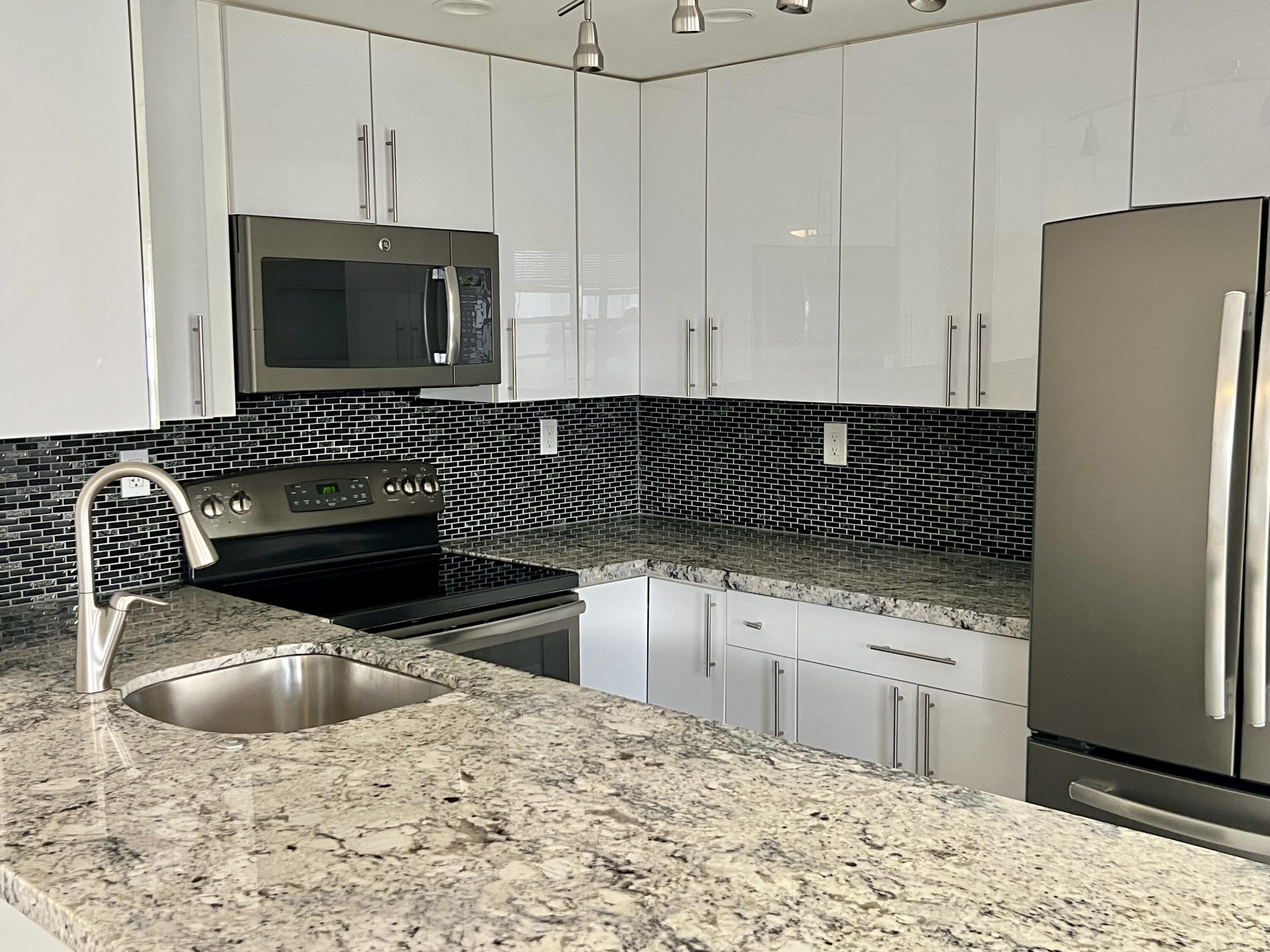 150 Burgandy Way, Unit D Delray Beach, FL 33484 - Photo 5 of 33 a kitchen with stainless steel appliances kitchen island granite countertop a stove a sink and a microwave