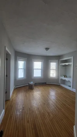a view of an empty room with window and wooden floor