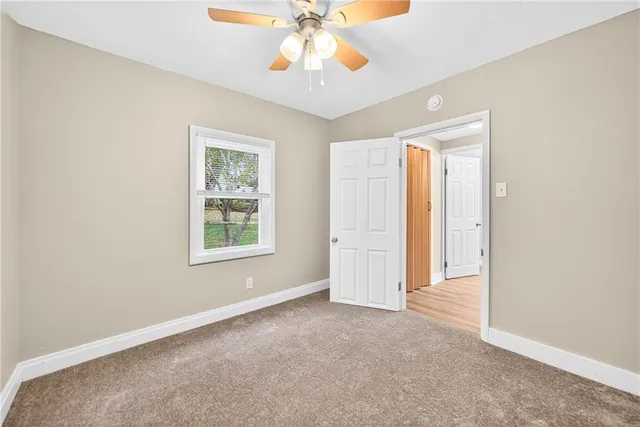 an empty room with chandelier fan and windows