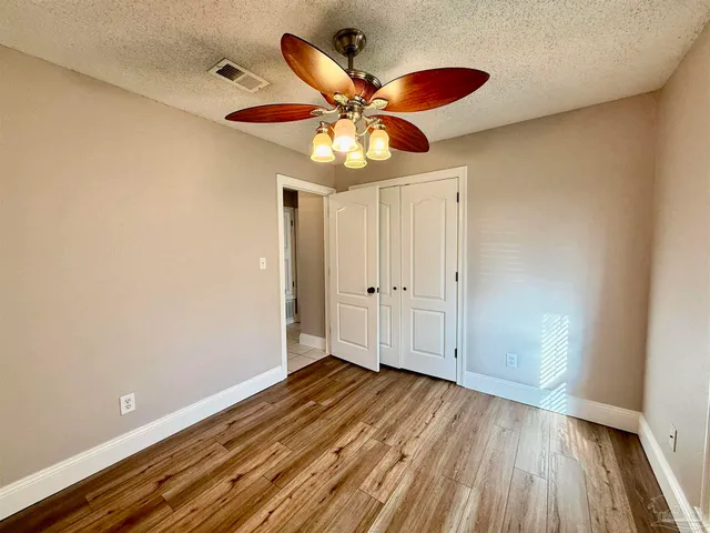 a view of an empty room with wooden floor and a ceiling fan
