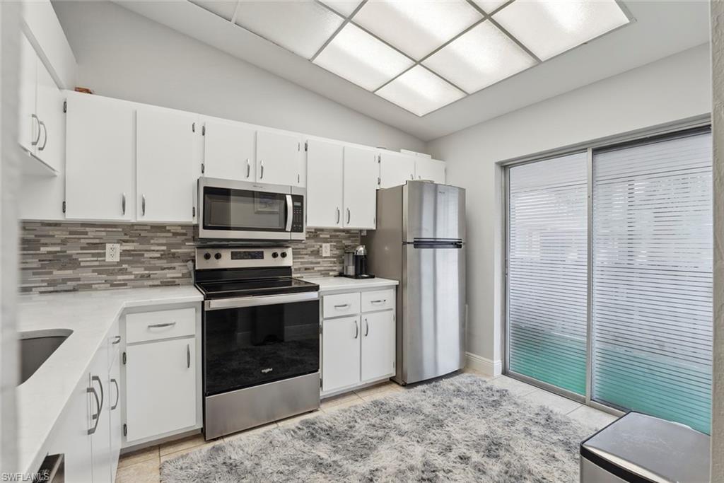 3410 Frosty Way, Unit 4802 Naples, FL 34112 - Photo 15 of 27 Kitchen with appliances with stainless steel finishes, light countertops, decorative backsplash, white cabinetry, and lofted ceiling