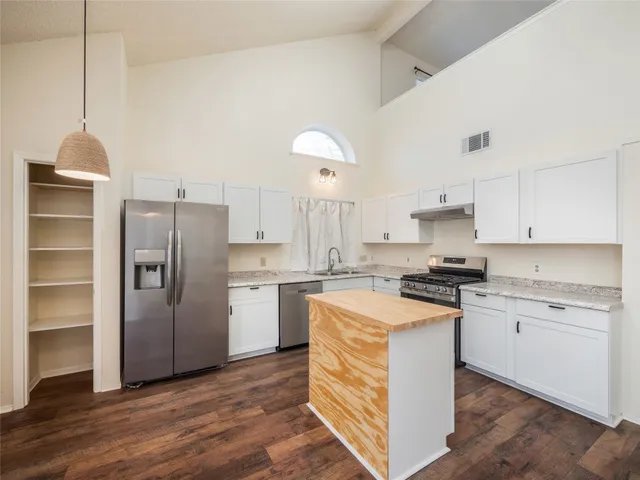 a kitchen with a refrigerator a stove a sink and white cabinets with wooden floor