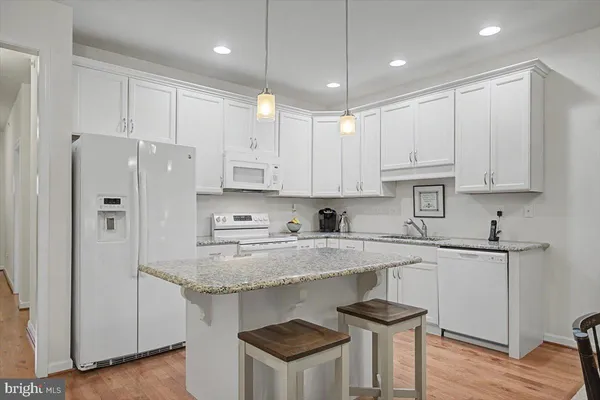 a kitchen with stainless steel appliances granite countertop a refrigerator a sink dishwasher a stove and white countertops with wooden floor