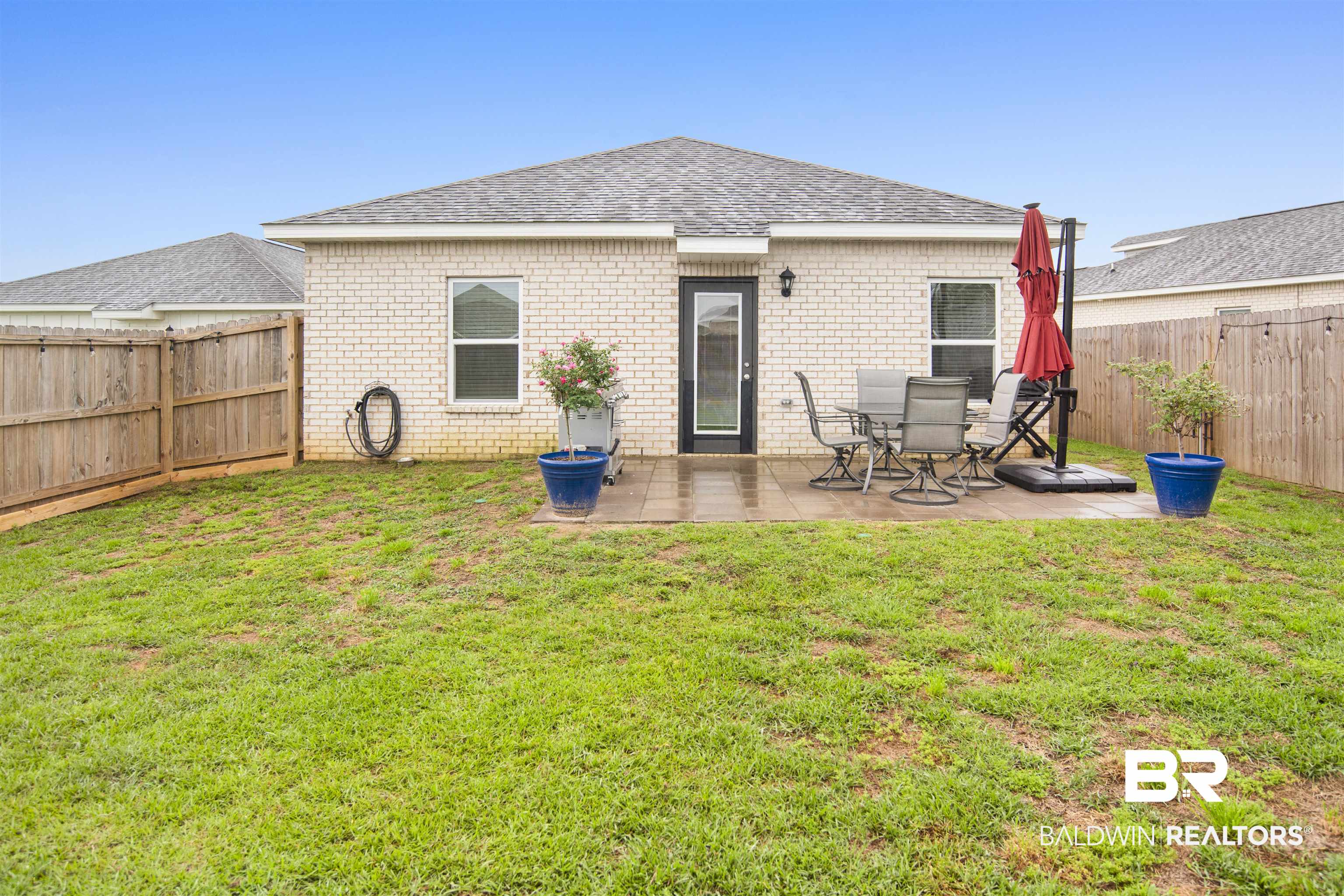 12813 Patriot Way Daphne, AL 36527 - Photo 20 of 23 Fenced backyard featuring a paver patio with a rear entry door, two windows, and light-colored brick exterior